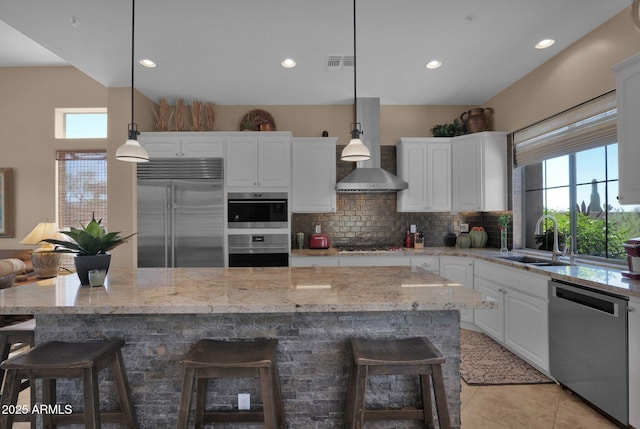 kitchen with stainless steel appliances, wall chimney exhaust hood, a sink, and white cabinets