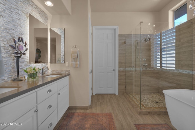 bathroom featuring a freestanding tub, wood finished floors, a sink, double vanity, and a stall shower