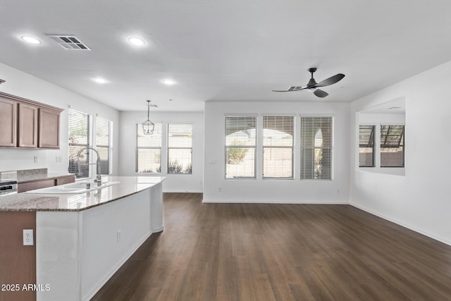 kitchen with sink, ceiling fan, hanging light fixtures, light stone countertops, and dark hardwood / wood-style flooring