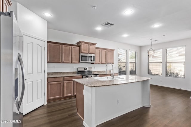 kitchen with an island with sink, sink, hanging light fixtures, stainless steel appliances, and dark wood-type flooring