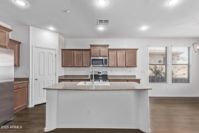 kitchen with appliances with stainless steel finishes, sink, dark hardwood / wood-style flooring, light stone countertops, and a center island with sink