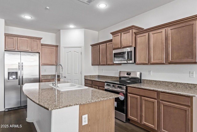 kitchen featuring appliances with stainless steel finishes, dark hardwood / wood-style floors, sink, light stone countertops, and a center island with sink