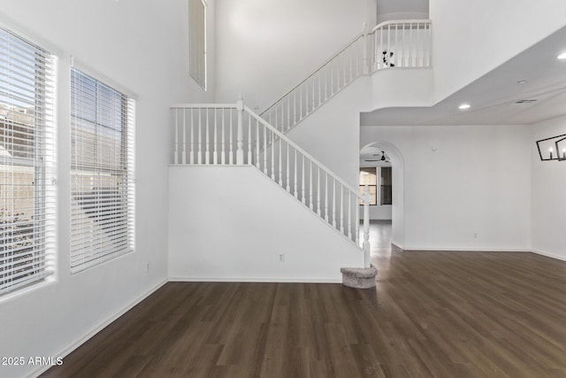 unfurnished living room featuring ceiling fan, dark hardwood / wood-style floors, a healthy amount of sunlight, and a high ceiling