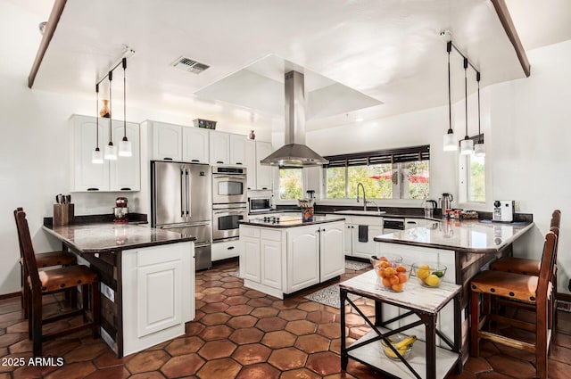kitchen with visible vents, island exhaust hood, a peninsula, dark countertops, and stainless steel appliances