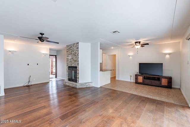 unfurnished living room with a stone fireplace, wood finished floors, a ceiling fan, and visible vents