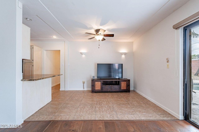 unfurnished living room featuring wood finished floors, baseboards, and ceiling fan