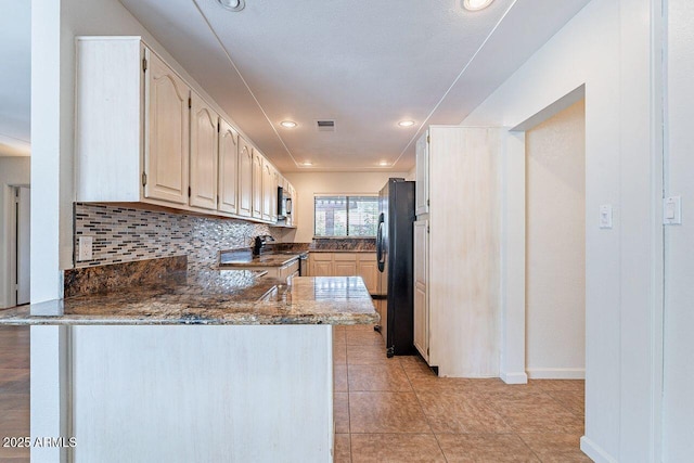 kitchen featuring visible vents, backsplash, a peninsula, freestanding refrigerator, and range