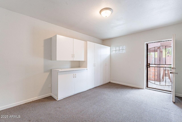 unfurnished room featuring light colored carpet, a textured ceiling, and baseboards