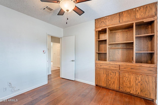 unfurnished bedroom with baseboards, wood finished floors, visible vents, and a textured ceiling