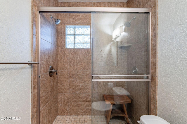 bathroom featuring a stall shower, toilet, and a textured wall