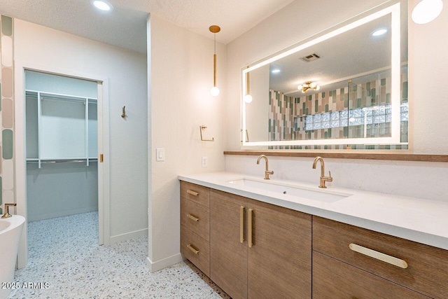 full bath with visible vents, a walk in closet, baseboards, vanity, and speckled floor