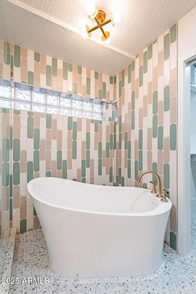 full bath with a freestanding bath, tile walls, speckled floor, and a textured ceiling