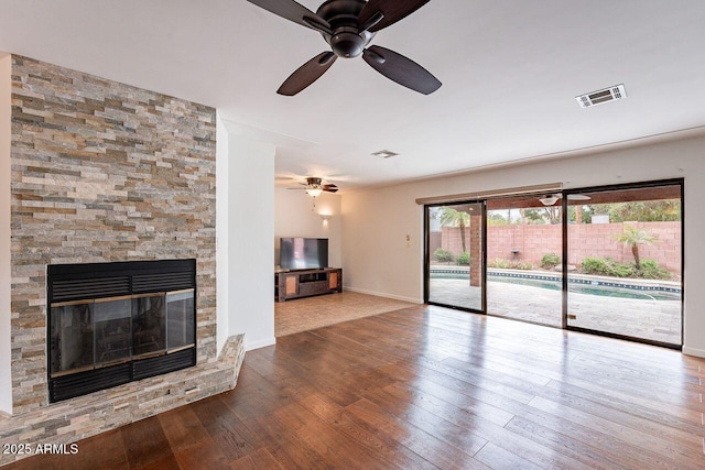 unfurnished living room featuring a stone fireplace, wood finished floors, visible vents, and baseboards