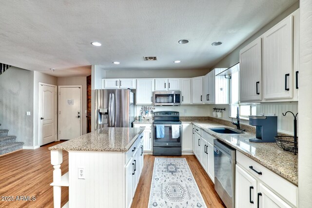 775 E Leslie Ave, San Tan Valley, AZ 85140 - kitchen with stainless steel appliances, a sink, light wood-style flooring, a center island, and light stone countertops