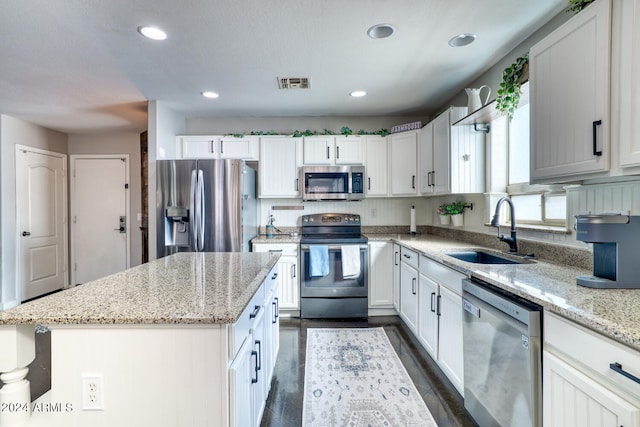 kitchen with sink, white cabinetry, light stone counters, a center island, and stainless steel appliances