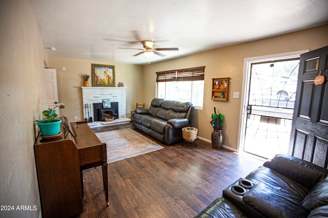 living room with dark wood-type flooring, a wood stove, and ceiling fan