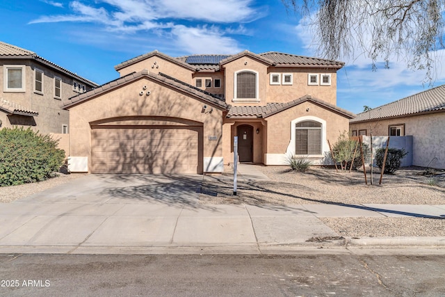 mediterranean / spanish-style house with a garage, solar panels, driveway, a tiled roof, and stucco siding