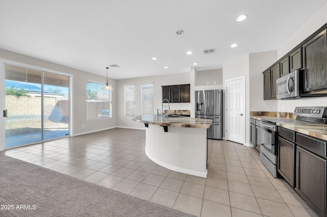 kitchen with a kitchen island with sink, stainless steel appliances, light countertops, a sink, and light tile patterned flooring