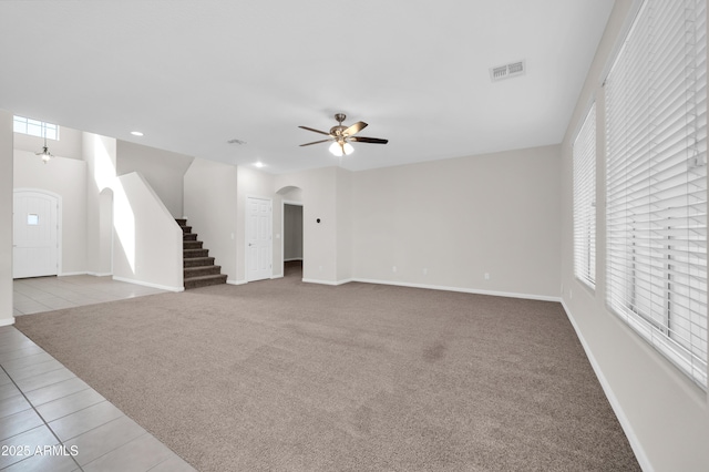 unfurnished living room with visible vents, arched walkways, light colored carpet, ceiling fan, and stairs