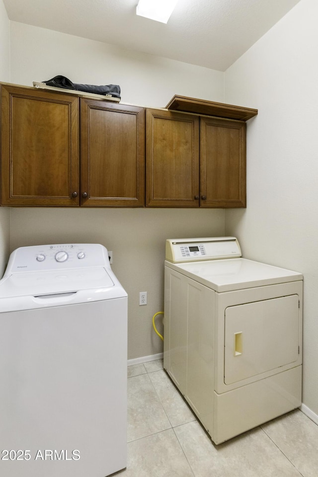 clothes washing area with cabinet space, washer and clothes dryer, baseboards, and light tile patterned floors