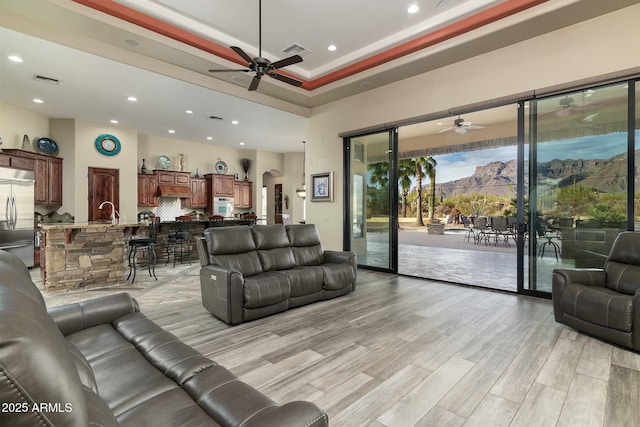 living room with ceiling fan, a raised ceiling, light wood-type flooring, and crown molding