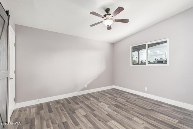 empty room with hardwood / wood-style flooring, vaulted ceiling, a barn door, and ceiling fan