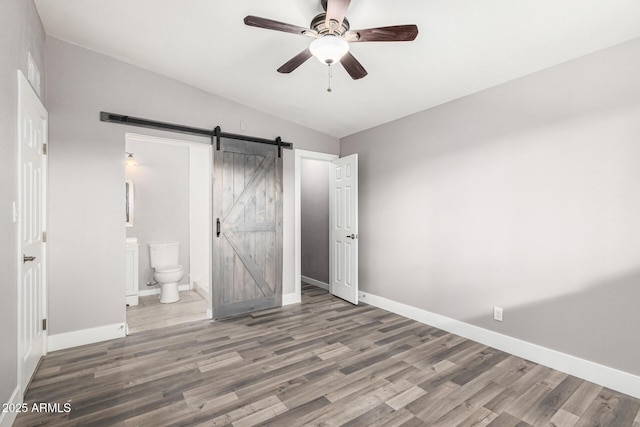 unfurnished bedroom with hardwood / wood-style flooring, a barn door, ceiling fan, and ensuite bathroom