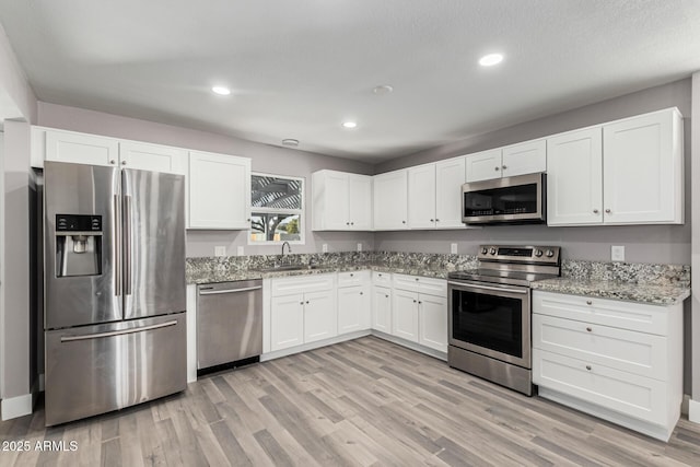 kitchen with white cabinetry, sink, light stone counters, light hardwood / wood-style floors, and stainless steel appliances