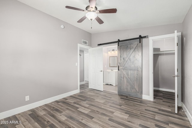 unfurnished bedroom with hardwood / wood-style flooring, a barn door, vaulted ceiling, and a closet