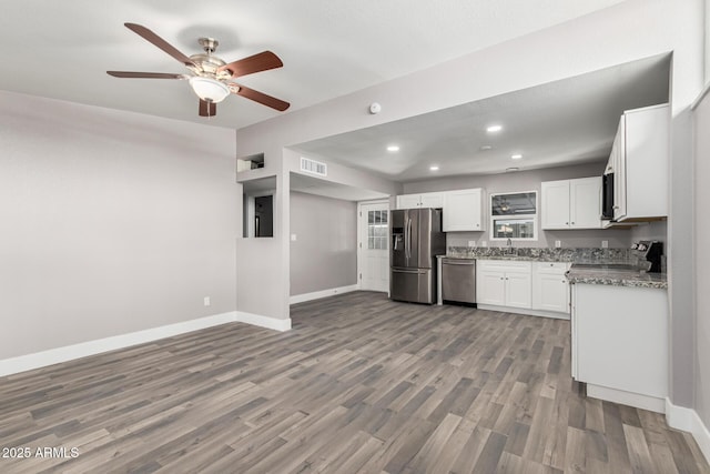 kitchen with sink, appliances with stainless steel finishes, white cabinetry, hardwood / wood-style floors, and light stone counters