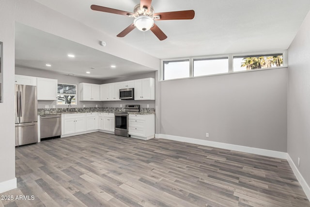 kitchen with sink, stainless steel appliances, light stone countertops, hardwood / wood-style floors, and white cabinets