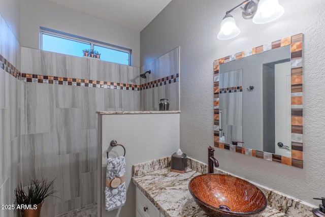 bathroom with tiled shower and vanity