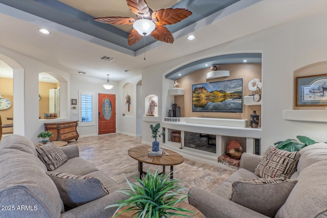 living room with ceiling fan, a fireplace, and a tray ceiling