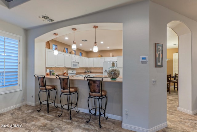 kitchen with white cabinetry, white appliances, kitchen peninsula, a breakfast bar area, and backsplash