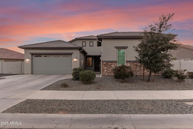 prairie-style house with a garage, driveway, stone siding, fence, and stucco siding