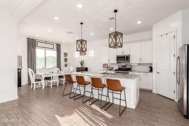 kitchen featuring a breakfast bar area, stainless steel appliances, wood finish floors, visible vents, and white cabinetry