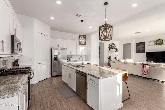 kitchen with a sink, visible vents, white cabinetry, open floor plan, and appliances with stainless steel finishes