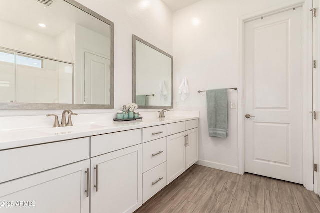 full bathroom with double vanity, a sink, baseboards, and wood finished floors