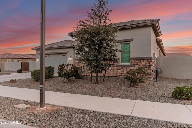 view of front of property with a garage, stone siding, fence, and stucco siding