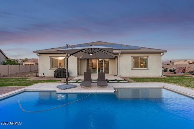 back of house at dusk featuring a patio area, solar panels, and stucco siding