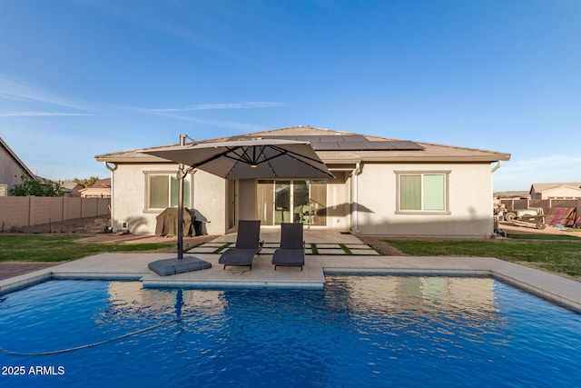 back of property with a fenced in pool, stucco siding, roof mounted solar panels, a patio area, and fence