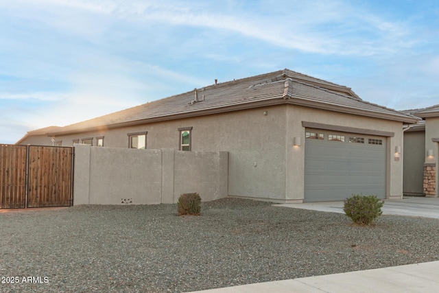 view of property exterior with stucco siding, an attached garage, fence, driveway, and a tiled roof