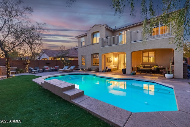 pool at dusk featuring a patio, an outdoor hangout area, and a lawn