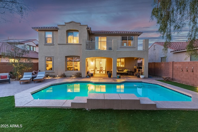 back house at dusk featuring a balcony, outdoor lounge area, a fenced in pool, and a patio