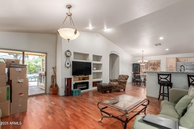living room featuring vaulted ceiling, a chandelier, built in shelves, and light wood-style flooring