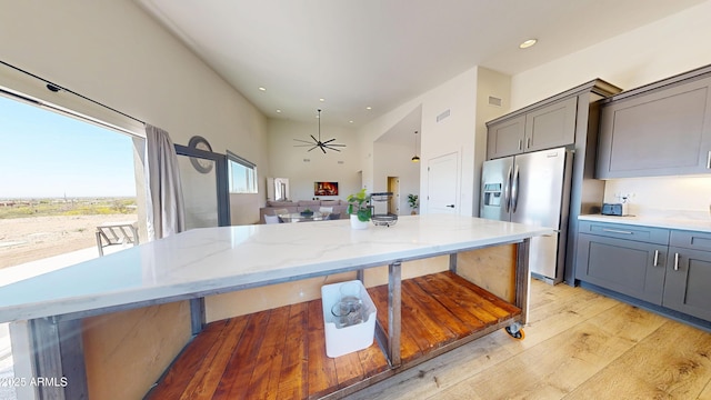 kitchen featuring stainless steel fridge with ice dispenser, light wood finished floors, light stone counters, gray cabinets, and recessed lighting