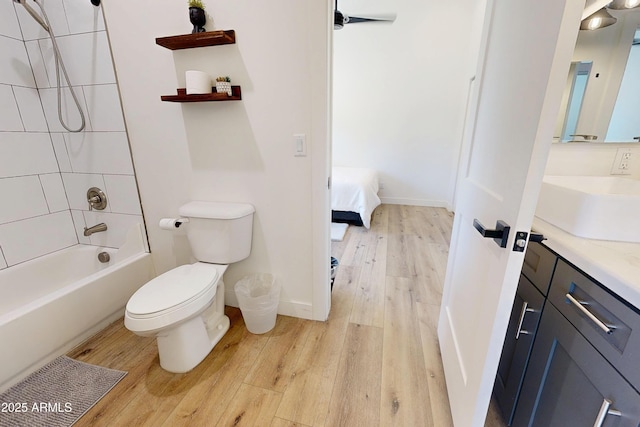 bathroom featuring wood finished floors, toilet, vanity, bathing tub / shower combination, and baseboards