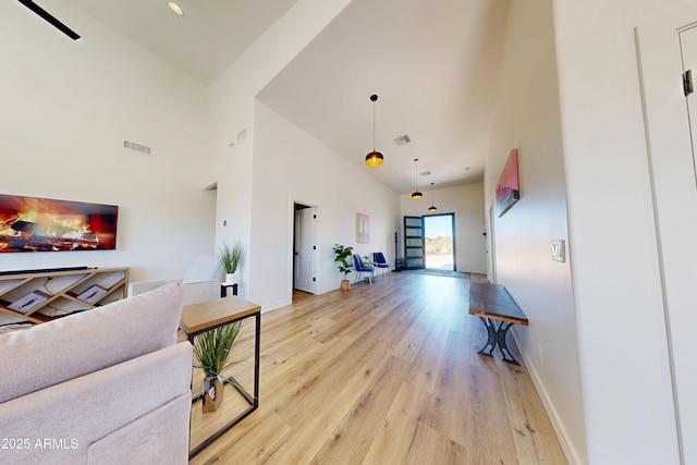 living area featuring light wood-style flooring, a towering ceiling, and baseboards