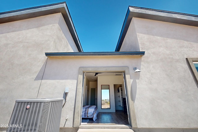 view of exterior entry with stucco siding and central AC