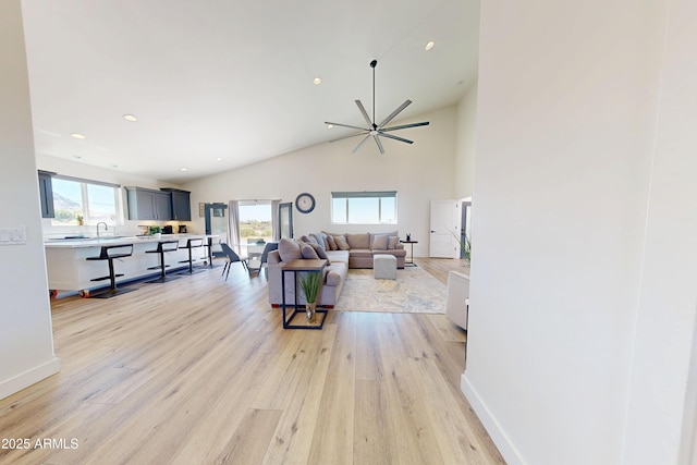 living room with light wood-style flooring, ceiling fan, recessed lighting, high vaulted ceiling, and baseboards